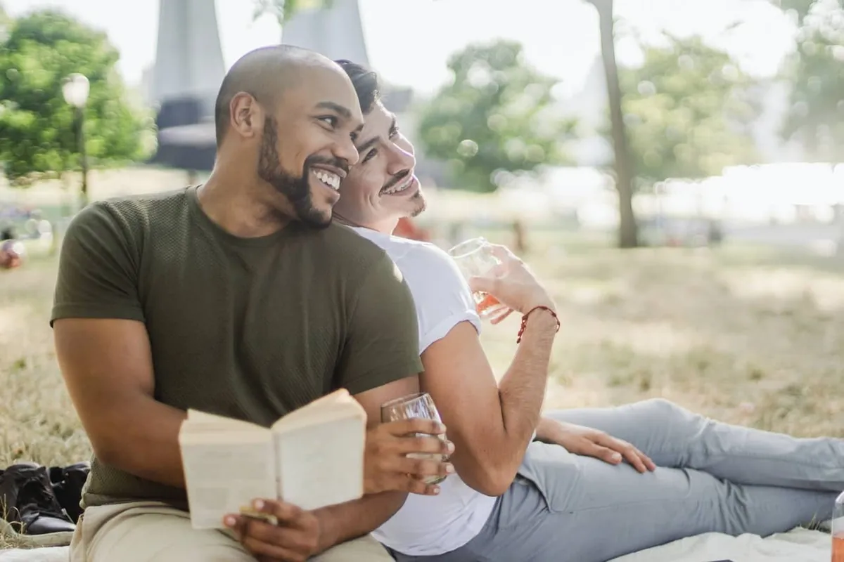 Zwei Männer sitzen entspannt auf einer Wiese, einer hält ein Buch