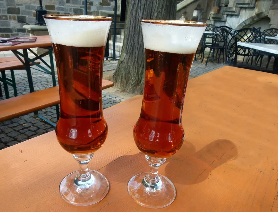 Zwei Biergläser auf einem Holztisch in einem Biergarten