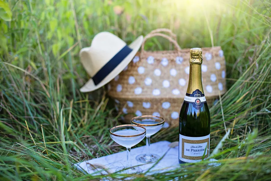 Picknick mit Sektflasche, zwei Gläsern und Strohhut im Gras